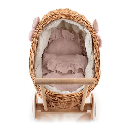 Carrozzina in vimini per bambole con rifiniture rosa, dotata di manico, cuscino e copertina.